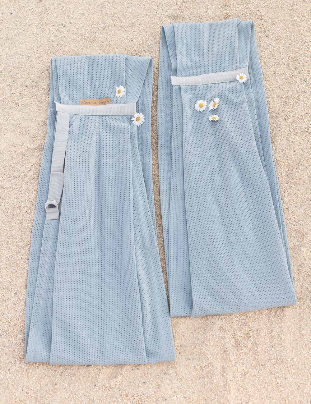 AQUA Loops in "ocean mit grauem Ripsband" liegen nebeneinander im Sand und sind geschmückt mit Gänseblümchen. 