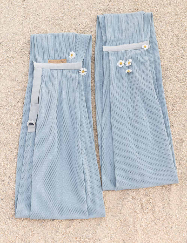 AQUA Loops in "ocean mit grauem Ripsband" liegen nebeneinander im Sand und sind geschmückt mit Gänseblümchen. 